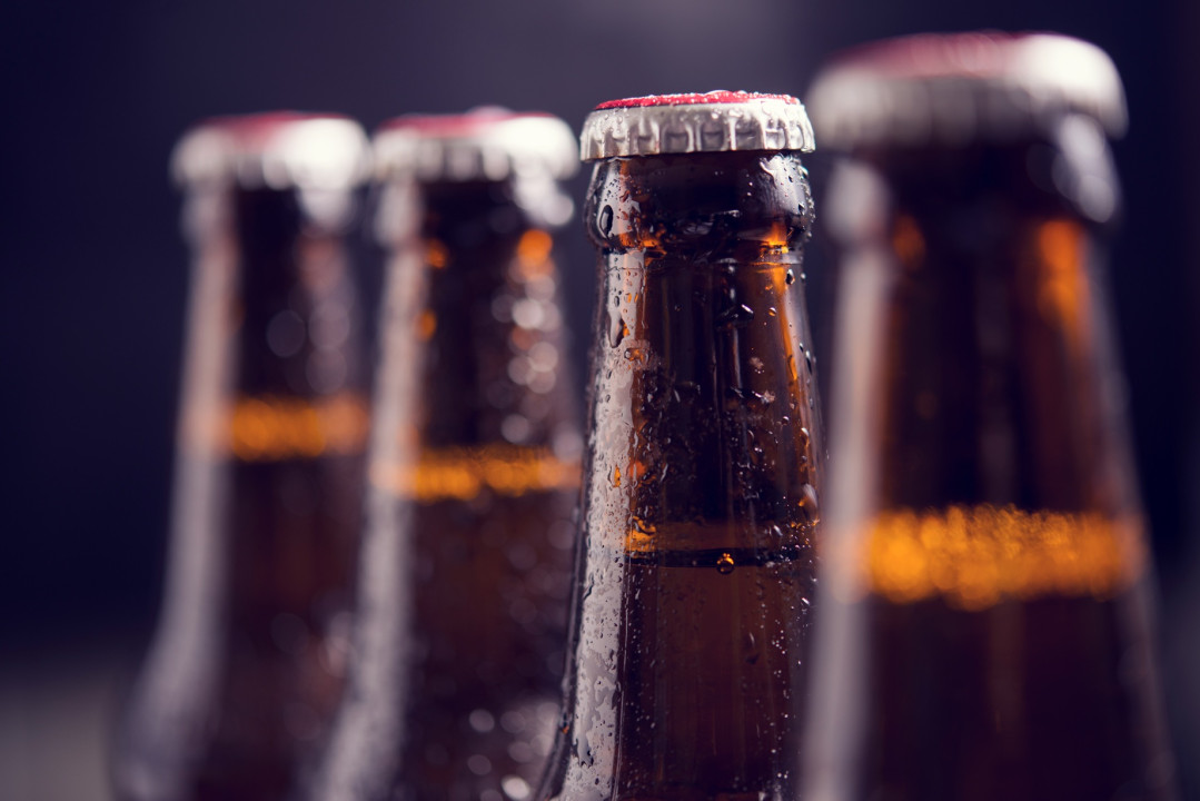 Glass bottles of beer with glass and ice on dark background